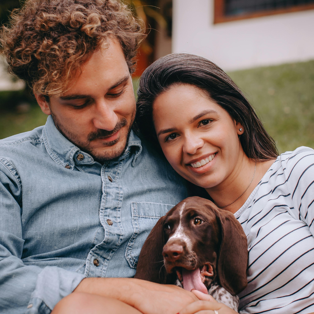 Man and woman sitting outdoors with a dog, smiling at the camera.